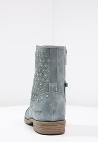 Bota de cuero gris hasta el tobillo con diseño floral perforado, acentos de tachuelas plateadas, un tacón bajo y cremallera lateral para un fácil acceso.