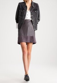 Zwarte denim jas over een witte blouse, gecombineerd met een grijze leren rok met een kleurgebroken zoom. Zwarte schoenen maken de look compleet.