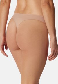 Alastus thong-alushousut, joissa on saumatonta muotoilua, pehmeää kangasta, minimalistinen leikkaus ja sileä pinta takana.