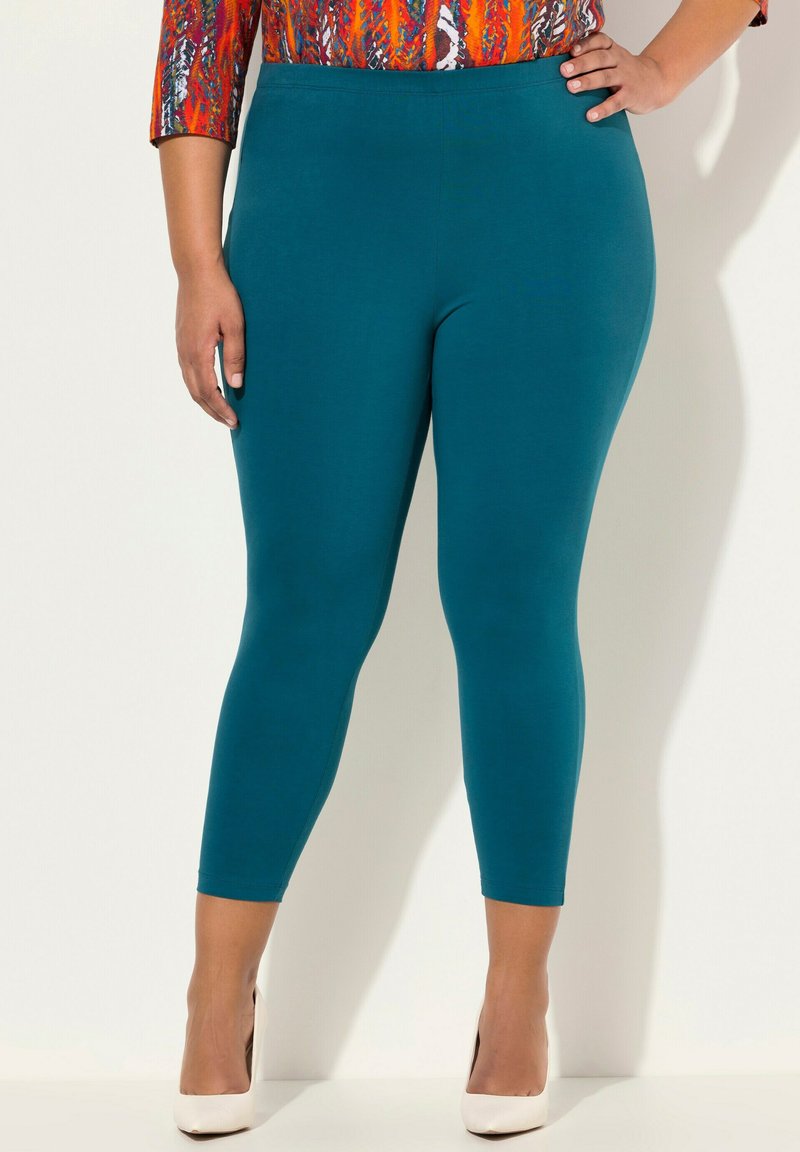 Leggings en color teal hechos de un material elástico, con un ajuste ceñido y longitud hasta los tobillos, combinados con tacones nude para un look completo.