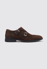 Zapato de monk strap de ante marrón con dos hebillas plateadas, punta redondeada y suela de goma negra. Textura suave y diseño limpio.