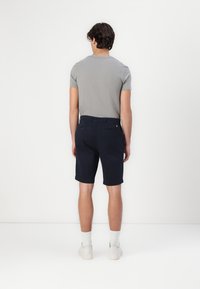 Celana pendek navy biru dengan tekstur halus, kantong samping, dan dua kantong belakang. Dipasangkan dengan kaos lengan pendek abu-abu dan sepatu sneakers putih.
