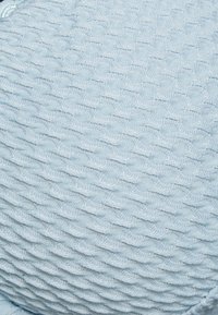 Almofada de malha em azul claro, com um padrão texturizado de ondas e uma aparência suave e tecida. Forma arredondada, costura detalhada.