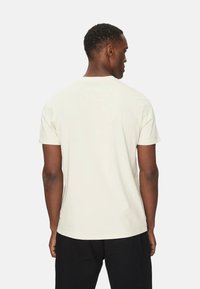Camiseta de manga corta color crema hecha de algodón, con cuello redondo y un corte relajado, con un diseño liso sin logotipos ni patrones visibles.