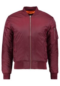 Giacca bomber color bordeaux realizzata in un materiale liscio e leggero. Presenta una zip frontale, polsini a coste e una tasca sul manica sinistra.