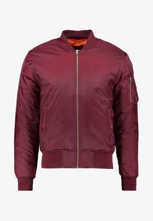 Chaqueta bomber de color burdeos, fabricada con material suave y ligero. Presenta un cierre frontal de cremallera, puños acanalados y un bolsillo en la manga izquierda.