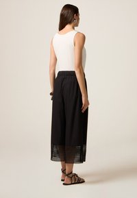 Witte mouwloze top gecombineerd met zwarte culottes met een perforate zoom, gedragen met zwarte sandalen met bandjes. Neutrale achtergrond.