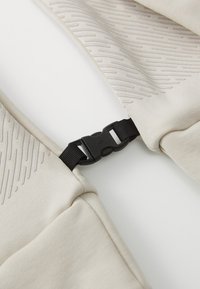 Bee�ž kangas tekstuuriga mustriga, millel on must plastikust pandlad. Kujundus on minimalistlik ja sellel on siledad servad.