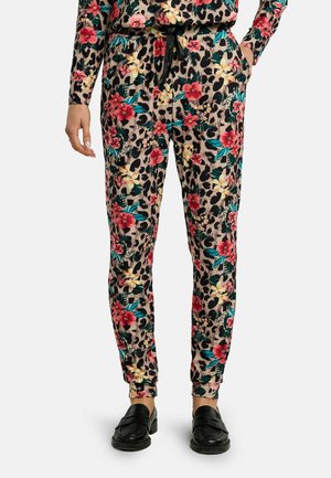 Virágos és leopárdmintás szűkülő fazonú nadrág húzózsinóros derékkal, fekete csúszásmentes cipővel és hozzáillő virágos felsővel viselve.