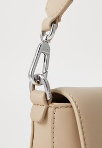 Sac en cuir beige avec une texture lisse et une forme arrondie, doté d'un fermoir en métal argenté et de la marque Calvin Klein sur les éléments en métal.