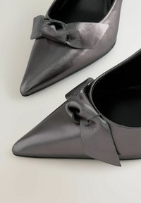 Fekete bőrből készült, hegyes orrú magassarkú cip�ő, elöl masnival díszítve. Sima textúra, elegáns, modern dizájn.