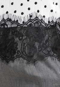 Un bordo in pizzo nero sovrapposto a un tessuto strutturato con pois bianchi e neri. Il design presenta intricati motivi floreali nel pizzo.