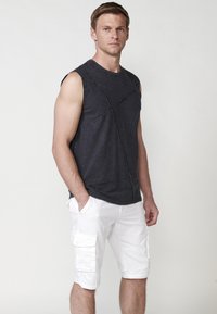 Top sans manches gris foncé avec un design en point de croix texturé ; associé à un short cargo blanc avec des poches latérales et des ourlets pincés.