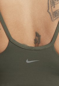 Persona che indossa una maglietta sportiva Nike verde oliva con tatuaggi visibili sulla parte superiore della schiena e sulle spalle.