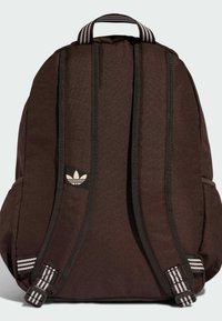 Brązowy plecak z tkaniny z czarnymi akcentami, ergonomiczne, wyściełane paski, górna rączka oraz małe logo z przodu. Paski ozdobione poziomymi paskami.
