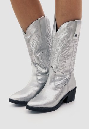 Botas de vaquero plateadas hechas de cuero metálico, con punteras puntiagudas, diseños embossados intrincados y un tacón bajo y grueso.
