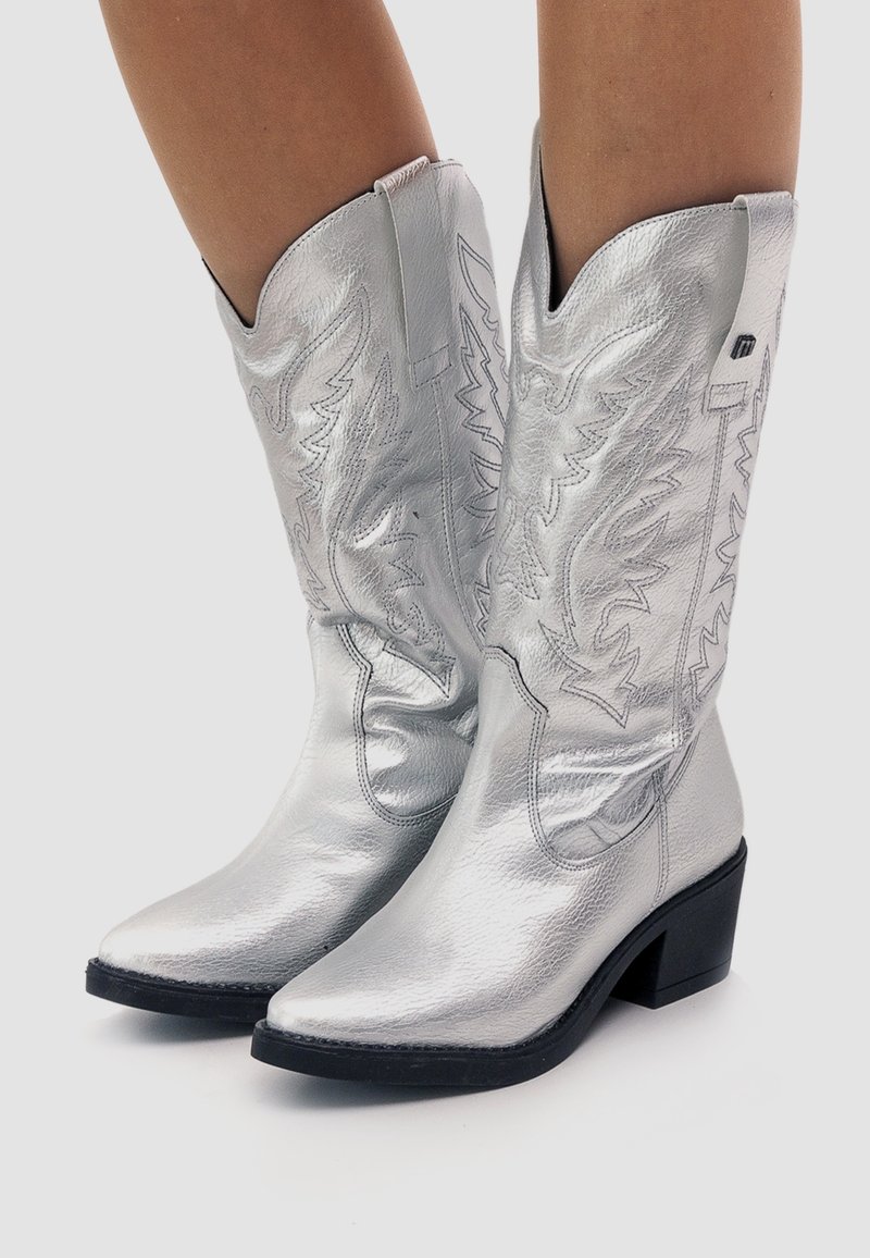 Botas de vaquero plateadas hechas de cuero metálico, con punteras puntiagudas, diseños embossados intrincados y un tacón bajo y grueso.