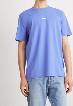 Mann trägt ein schlichtes blaues Kurzarm-T-Shirt mit dem Schriftzug "BOSS" auf der Brust und hellblaue Denim-Jeans.