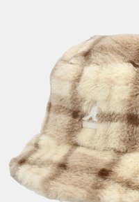 Cappello a secchiello in pelliccia sintetica con motivo a quadretti in tonalità beige e marrone. Presenta un logo ricamato bianco. Texture morbida e forma arrotondata.