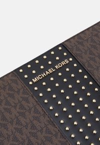 Brun mønstret håndtaske med gyldne nitter og et gyldent "Michael Kors" logo på en sort læderdetalje. Tekstureret materiale med kontrasterende elementer.