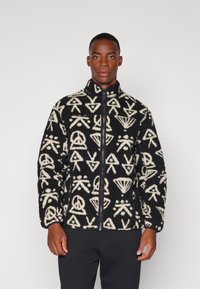 Jachetă din fleece negru cu modele abstracte crem, fermoar întreg, guler înalt și mâneci lungi. Textură moale și croială lejeră.