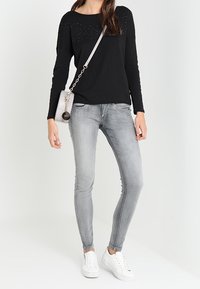 Top negro de manga larga con acentos de tachuelas, combinado con jeans ajustados grises y zapatillas blancas, accessorios con un pequeño bolso cruzado gris.