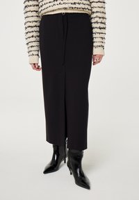 Zwarte, middellange rok van soepel materiaal, met een voorkruising en een verstelbare strik. Draag het met glanzende zwarte enkelboots.