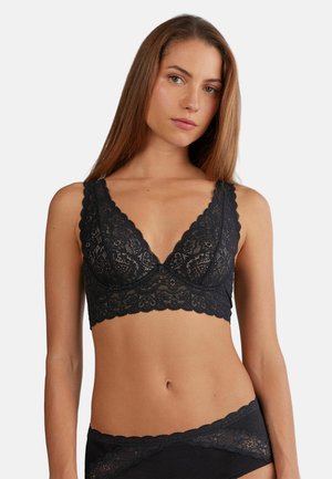 Bralette en dentelle noire avec des bonnets triangulaires, des bords festonnés et des bretelles larges. Présente des motifs floraux complexes et une finition douce et texturée.