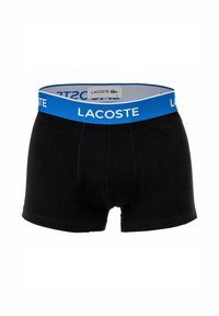 Boxer in cotone nero con una fascia elastica blu con la scritta "LACOSTE" stampata in bianco e un'etichetta con il logo sul retro.