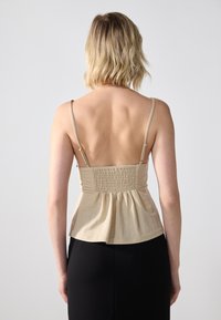 Beige tank topp med tynne stropper, med en samlet bakdel og en avslappet, utsvingt silhuett. Glatt tekstur med et mykt, lett materiale.
