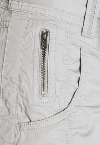 Tasca in tessuto grigio chiaro con una zip argentata visibile, cuciture dettagliate e una superficie leggermente testurizzata, progettata per una conservazione sicura.