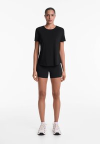 Black short-sleeve shirt and black shorts made of a smooth, stretchy material. Model wears light-colored athletic shoes. Simple design, no patterns.