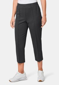 Schwarze, gerippte, kürzere Hosen mit einem elastischen Bund und vorderen Falten, kombiniert mit weißen Sneakers mit strukturierten Akzenten.