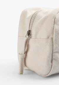 Pochette in tela color avorio, con zip superiore, hardware in metallo e superficie texturizzata. Include un anello in tessuto per il trasporto.