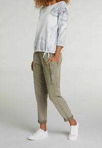 Jersey de color gris claro con diseño de cachemira y adornos sutiles, combinado con pantalones verde oliva de corte estrecho con cremalleras laterales y bolsillos.