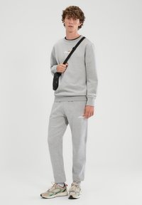 Conjunto de sudadera y pantalones deportivos gris hecho de algodón con puños acanalados, con un pequeño logo. Combinado con zapatillas deportivas multicolores.