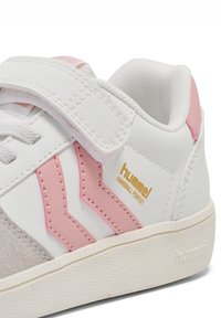 Białe sneakersy z różowymi akcentami, wyposażone w rzep, teksturowaną szarą zamszową cholewkę, złote logo oraz gumową podeszwę z wzorzystą powierzchnią.
