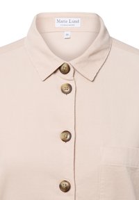Camicia beige con colletto e bottoni, presenta quattro bottoni tondi di colore chiaro e una tasca sul petto; tessuto testurizzato con leggere righe.