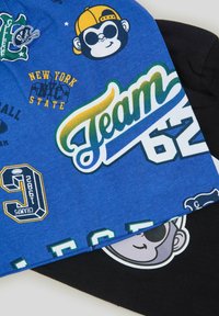 Due t-shirt di cotone; una blu con grafiche che includono una scimmia, "Team 62" e numeri, e una nera con un volto sorridente.