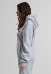 Pilkos gobtuvas su minkšta medžiaga. Su kengūros kišene ir rausvais švelnumais. Logotipas atspausdintas priekyje ir gale.