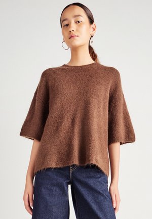 Maglione marrone, di taglio ampio con maniche corte, realizzato in materiale morbido e strutturato; l'orlo appare leggermente sfilacciato; abbinato a jeans blu scuro.