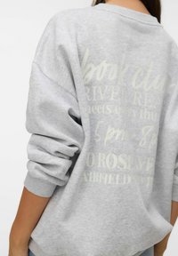 Pelēks džemperis ar brīvu piegriezumu, platiem piedurknēm un minimālistisku tekstu dizainu aizmugurē. Mīksta tekstūra ar ribotām aproču detaļām.