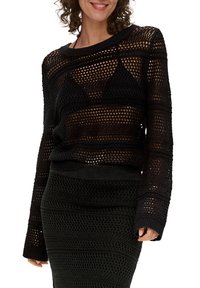 Czarny sweter dzianinowy z otwartym splotem, długimi rękawami i szerokim dekoltem, zestawiony z dopasowaną, teksturowaną spódnicą ołówkową.