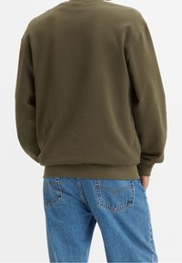 Felpa verde oliva con colletto rotondo e maniche lunghe; tessuto morbido; abbinata a jeans in denim blu chiaro con dettagli delle tasche cuciti.