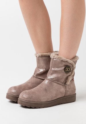 Bottines brunes courtes avec une texture brillante, bordées de fourrure en haut et à bout rond. Présente un logo circulaire sur le côté extérieur.