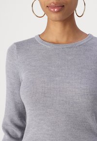 Haut gris à manches longues côtelé avec un col rond, présentant une texture douce et un léger extensibilité pour le confort. Style rond et ajusté.