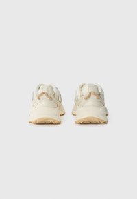 Lichtgekleurde sneaker met een gemêleerde mesh bovenkant, beige accenten, een gevoerde zool en een gemusterd profiel voor grip.