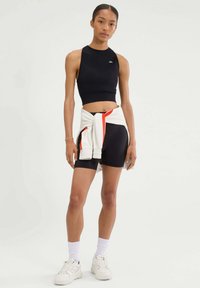 Czarny bezrękawnik crop top z wysokim kołnierzem; czarne szorty z białymi i pomarańczowymi akcentami; biały sweter związany w talii; białe trampki.