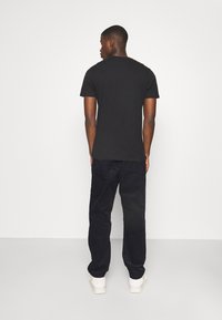 Camisa de algodón negra con cuello redondo, combinada con pantalones holgados azul oscuro. El conjunto se completa con zapatillas blancas.