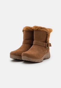 Bottines en daim marron avec un revers en fausse fourrure, détail de boucle sur le côté, et une semelle en caoutchouc texturé pour l'adhérence.